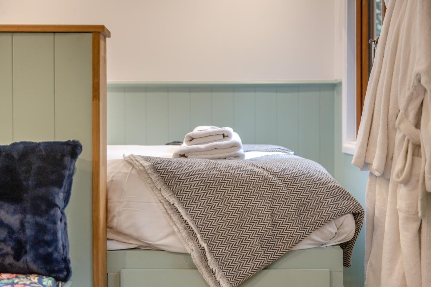 A bedroom with a bed, a bedside table, a window, and a towel rack.