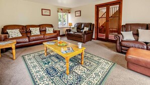 A living room with a brown leather sofa set, a wooden coffee table with magazines and fruit, a patterned rug, and a staircase leading to an upper floor. - 3 Bed in Two Waters Foot (oc-l29857) (Broadoak)