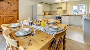 A dining area with a wooden table set for four, surrounded by chairs. A kitchen with white cabinets and appliances is visible in the background. - 3 Bed in Two Waters Foot (oc-l29857) (Broadoak)