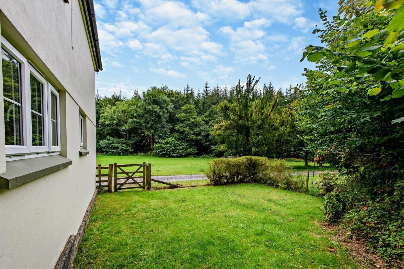 Une maison avec une pelouse bien entretenue, un portail en bois et de grands arbres en arrière-plan.