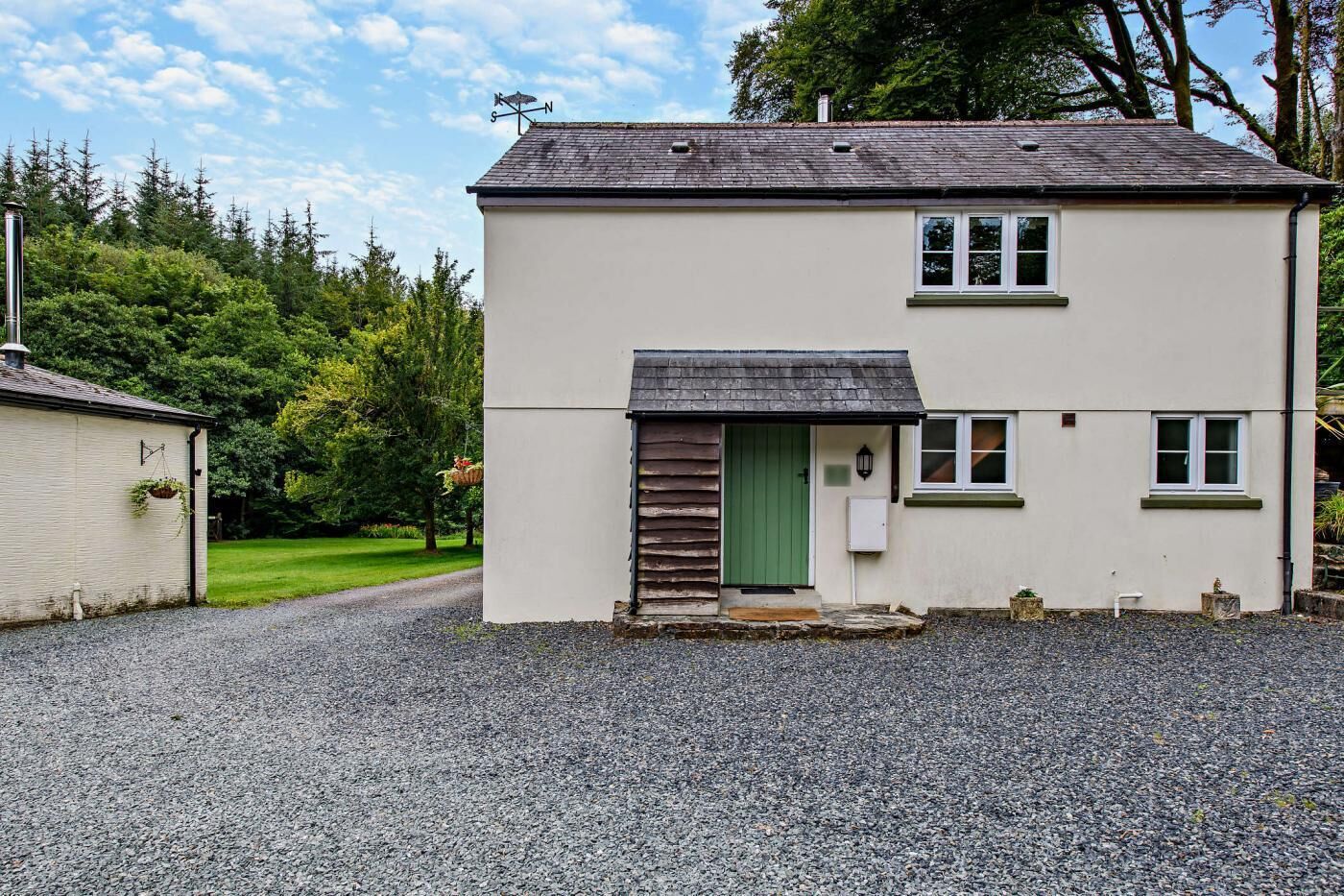 A two-story house with a gravel driveway, a green door, and a small porch area.
