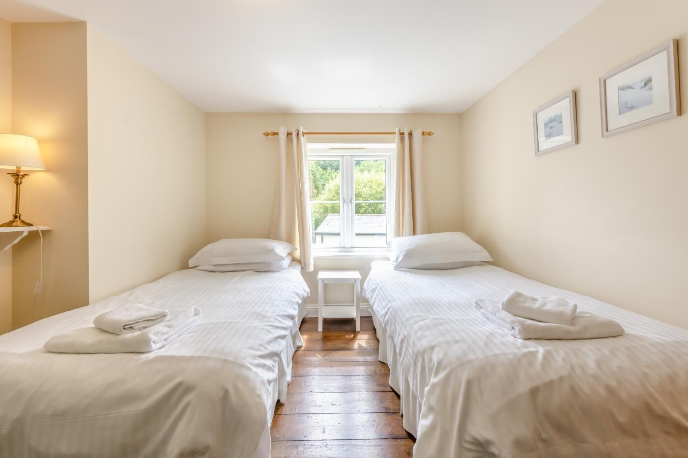 A twin room with two beds, a small table, a lamp, and a window with curtains.