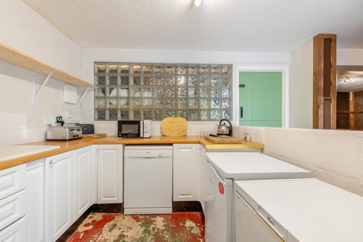 A compact kitchen with white cabinets, a microwave, a toaster, and a wooden cutting board.