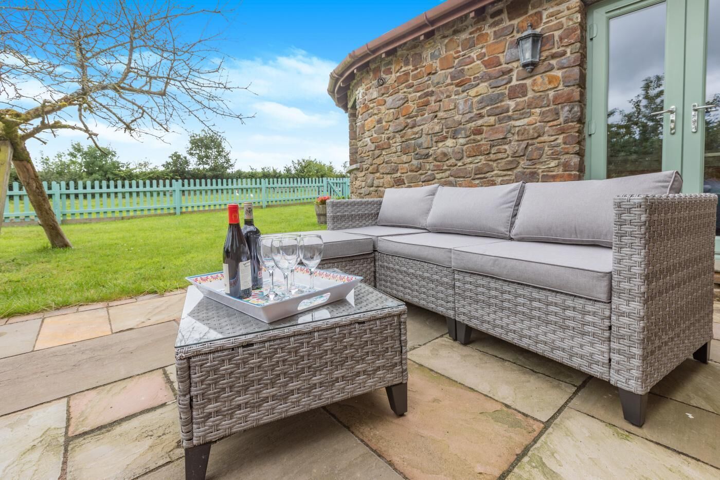 Eine Terrasse mit einem Korbsessel, einem kleinen Tisch und einem Tablett mit Weinflaschen und Gläsern.