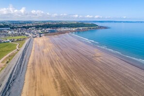 An aerial view of a coastal area with a wide sandy beach, a small town in the background, and a clear blue sky. - 2 Bed in Langtree (oc-b29908) (Langtree)