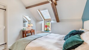 Une chambre avec un plafond en pente, un puits de lumière, une table de chevet avec une lampe et un lit avec des oreillers.