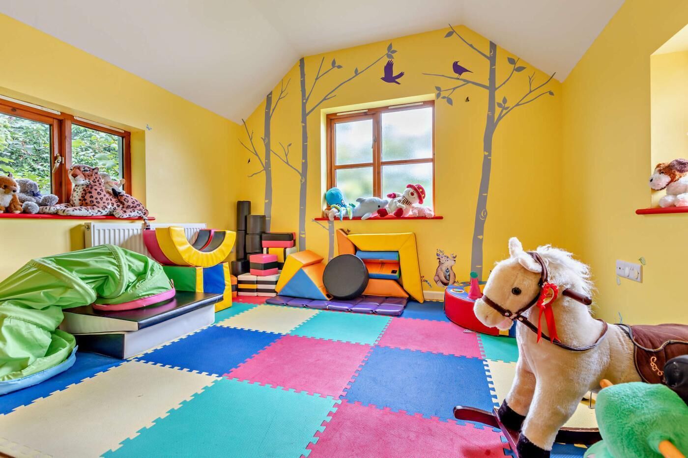 Une salle de jeux pour enfants avec un sol coloré, des jouets et une fenêtre.