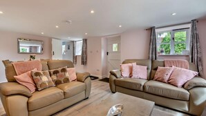 Una sala de estar con dos sofás de cuero color beige, cada uno decorado con cojines rosa y marrón. Una mesita de centro con una cuchara de plata se encuentra al frente.