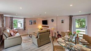 Una sala moderna con un conjunto de sofá, una mesa de comedor para dos personas, un televisor de pantalla plana y vistas al exterior.