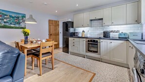 Une cuisine moderne avec des meubles blancs, un coin repas avec une table et des chaises en bois, et un tableau accroché au mur.
