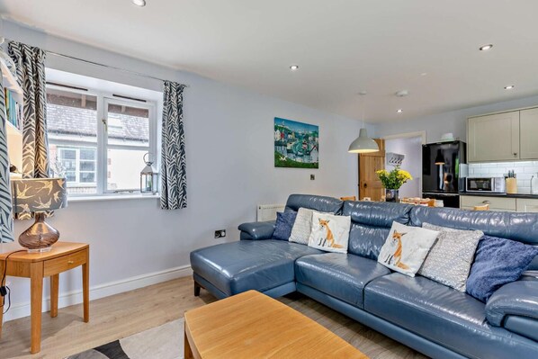 A modern living room with a blue leather sofa, wooden coffee table, and a dining area. - 2 Bed in Langtree (oc-e29913) (Langtree)
