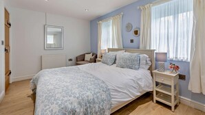 Une chambre à coucher avec un grand lit, une chaise, une table de chevet avec une lampe et une fenêtre avec des rideaux.
