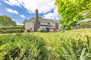 A house with a stone chimney, a lawn, and a garden with various plants. - 4 Bed in Molland (oc-w29835) (Molland)