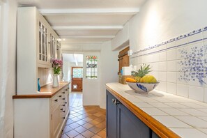 A narrow kitchen with a wooden countertop, a bowl of fruit, and a stained glass window. - 4 Bed in Molland (oc-w29835) (Molland)