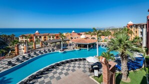 Área de piscina de un resort con piso a cuadros, sillones de descanso y vista al océano.