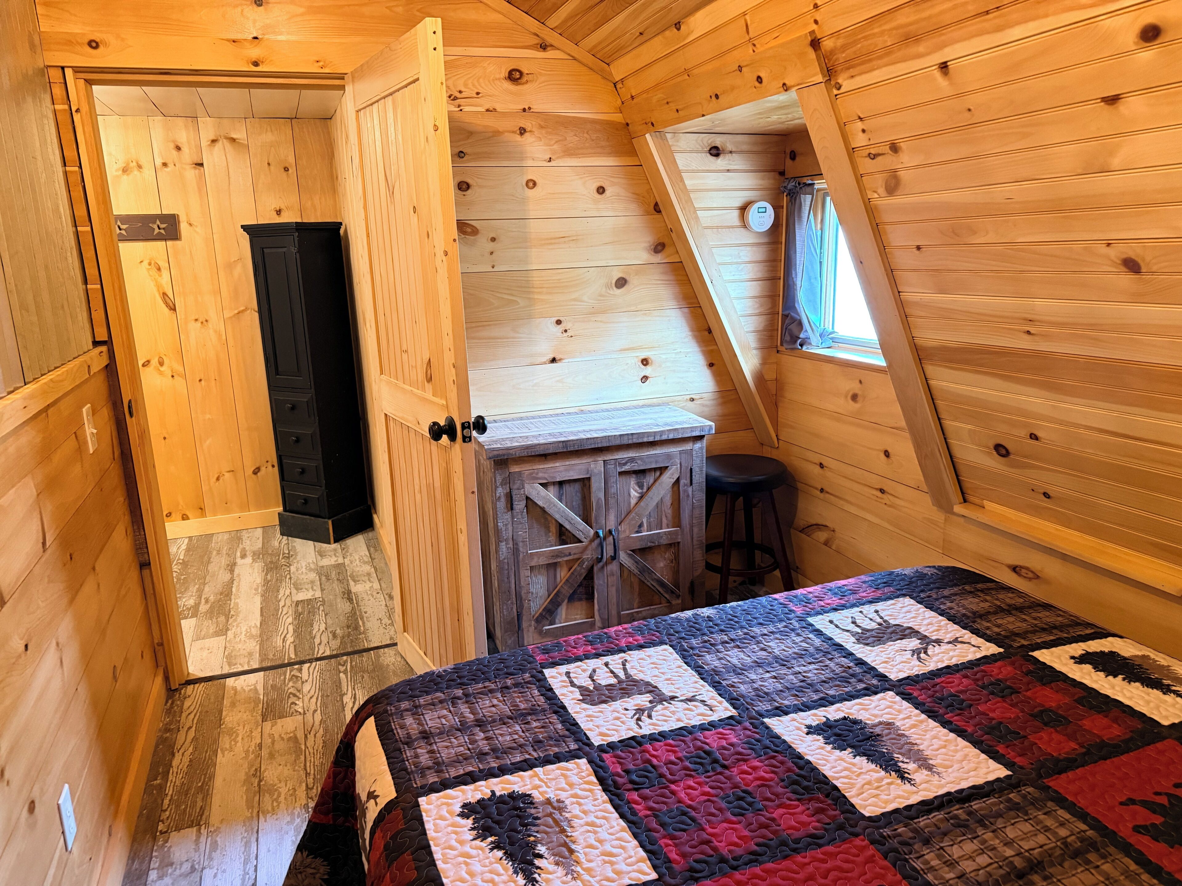 A cozy cabin room with a wooden interior, a bed with a quilt, a small table, and a door leading to another room.