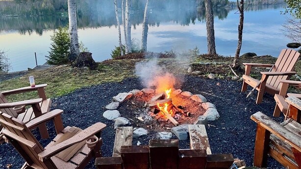 A lakeside outdoor seating area with a fire pit, surrounded by Adirondack chairs.