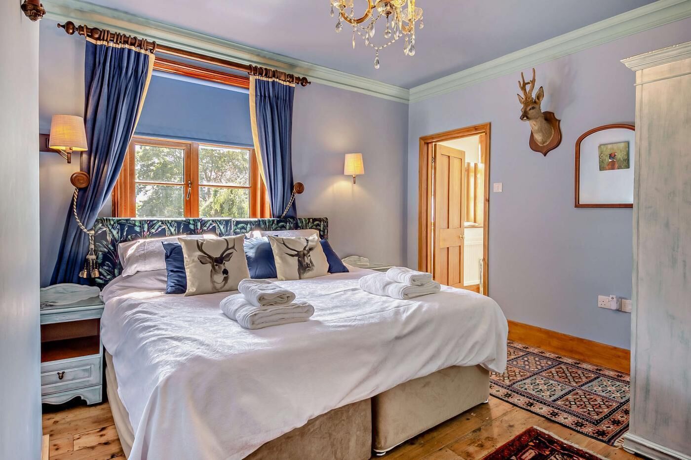 Ein Schlafzimmer mit einem großen Bett, blauen Vorhängen, einer Kristallleuchtre und einem Hirschgeweih an der Wand.