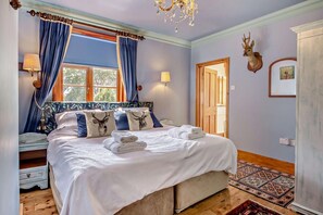 A bedroom with a large bed, blue curtains, a chandelier, and a deer head on the wall.