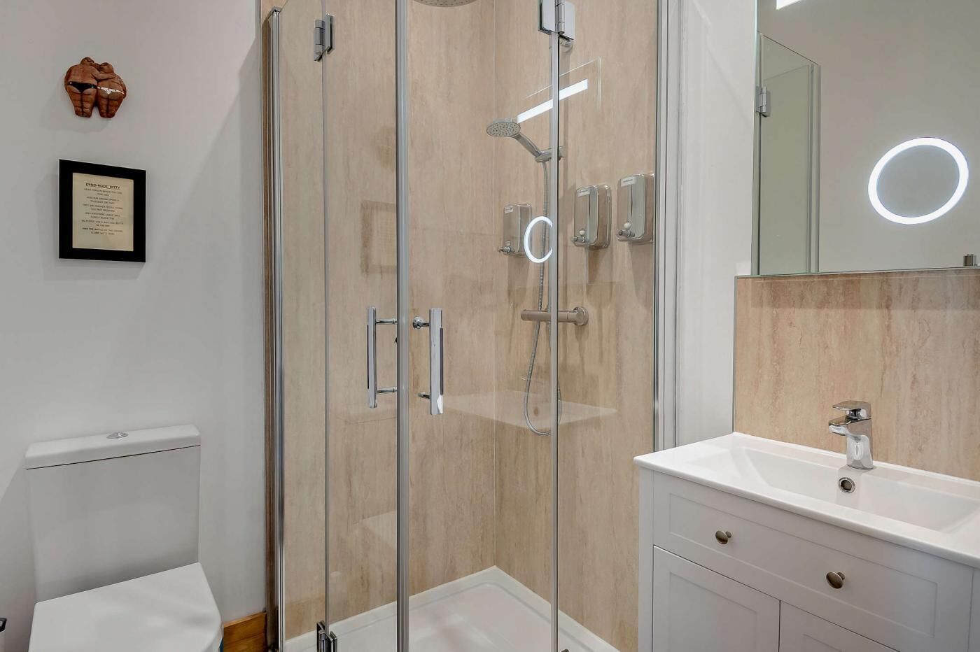 A modern bathroom with a glass-enclosed shower, a white sink, and a mirror with a circular light.