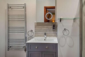 A bathroom with a towel rack, a mirror with a light, a sink, and a glass shelf.