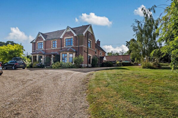 A large brick house with a gravel driveway and a well-maintained lawn.