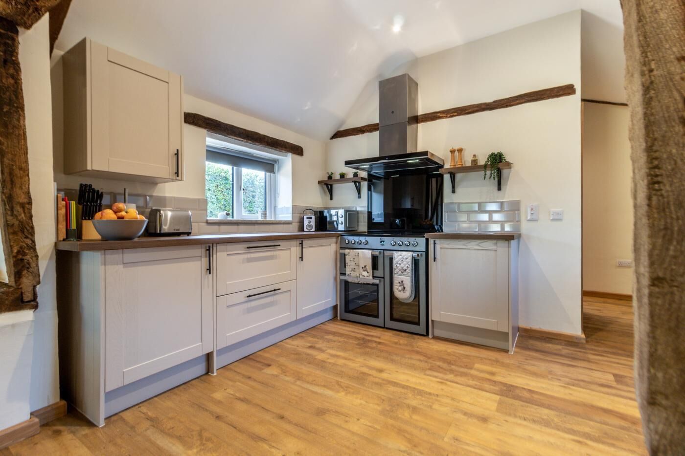 A modern kitchen with wooden flooring, a built-in oven, and a window providing natural light.