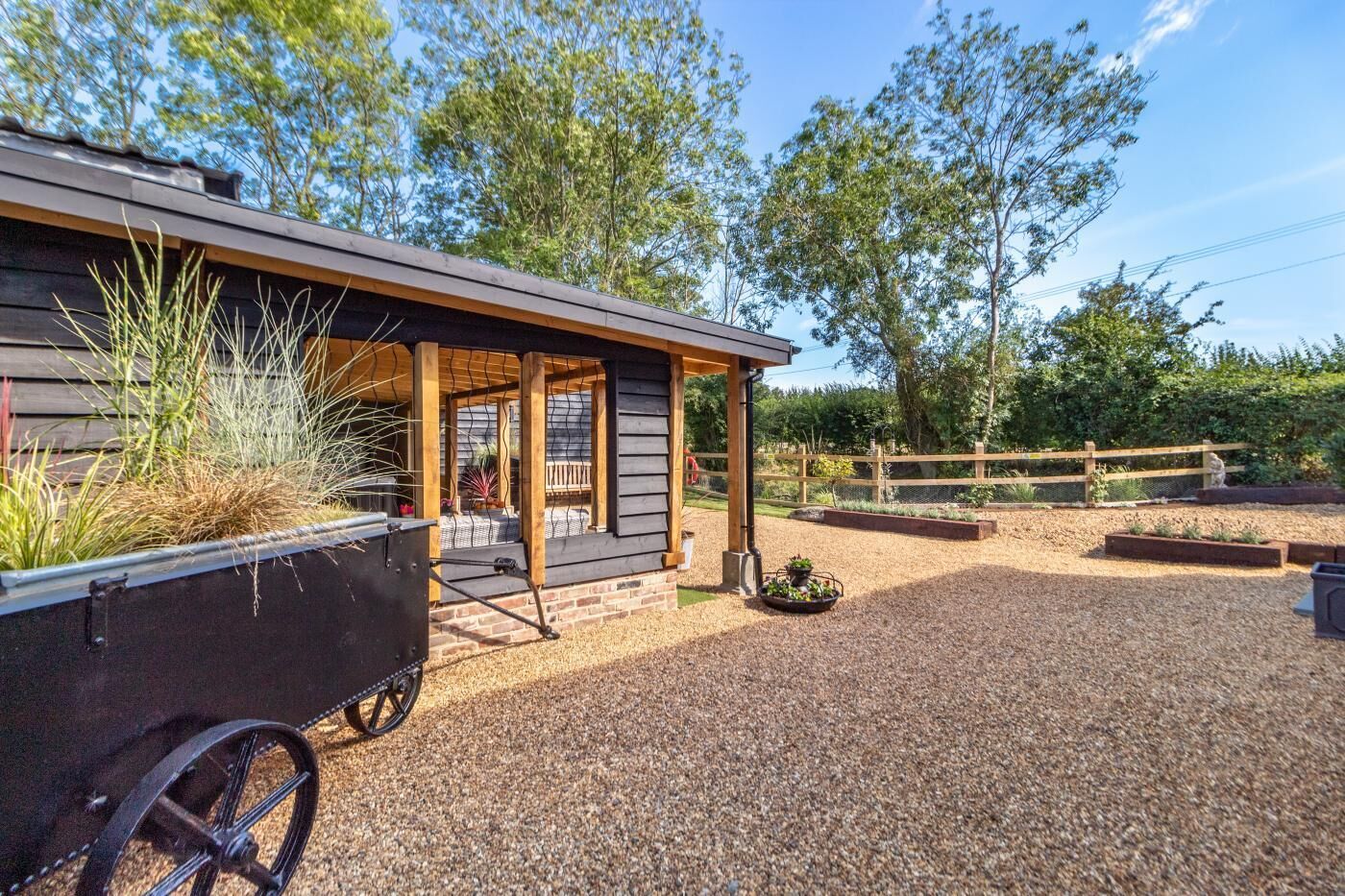 A rustic cabin with a covered porch, gravel driveway, and a fenced garden area.