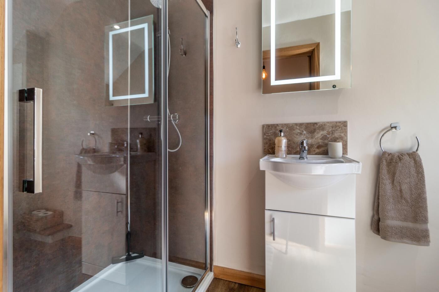 A modern bathroom with a glass-enclosed shower, a white sink with toiletries, and a towel rack.