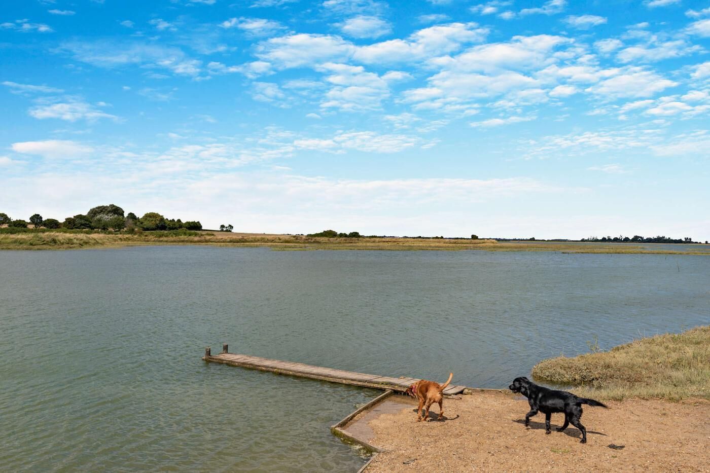 Un lac paisible, avec une jetée en bois qui s’avance sur l’eau, entouré de vastes champs et sous un ciel dégagé.