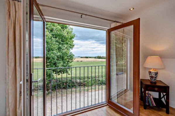 A room with a large sliding glass door leading to a balcony with a view of a grassy field and trees. - 1 Bed in Kirby-le-Soken (oc-f29905) (Kirby le Soken)