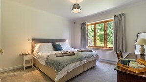 Un dormitorio con cama, mesita de noche, lámpara, ventana, cortinas y una bandeja con objetos.