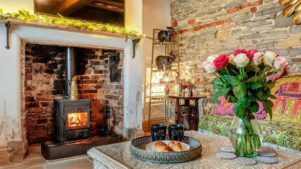 Una habitación acogedora con chimenea de ladrillo, un espejo decorativo y una mesa con un florero y un plato de cruasanes.