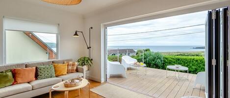 A modern living room with a sofa, coffee table, and a view of the sea through a glass door.