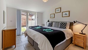 Une chambre à coucher avec un lit, des tables de chevet, un bureau et une vue sur l’extérieur.