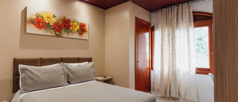 Un dormitorio con cama, mesita de noche, un cuadro, una puerta y una ventana con cortinas.