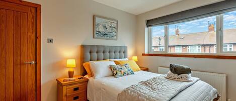 A bedroom with a large bed, wooden wardrobe, bedside tables, a window with a view, and a painting on the wall.