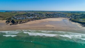 An aerial view of a coastal town with a sandy beach, clear blue waters, and a residential area with houses.