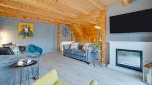 A wooden interior with a sofa, a small table, a TV, and a fireplace.