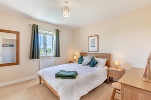 A bedroom with a large bed, bedside tables, a desk, a mirror, and a window with curtains. - 4 Bed in Beadnell (oc-s29958) (Beadnell)