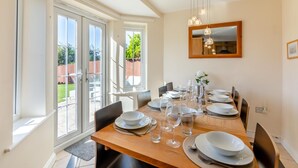 A dining area with a wooden table set for six, large windows, and a mirror on the wall. - 4 Bed in Beadnell (oc-s29958) (Beadnell)
