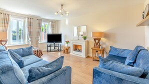 A living room with a fireplace, a television, and two blue sofas. - 4 Bed in Beadnell (oc-s29958) (Beadnell)