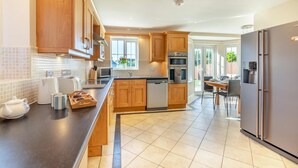 A modern kitchen with wooden cabinets, a stainless steel refrigerator, and a dining area with a table and chairs. - 4 Bed in Beadnell (oc-s29958) (Beadnell)
