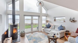 Ein geräumiges Wohnzimmer mit großem Fenster, Kamin, Sofa und Meerblick.