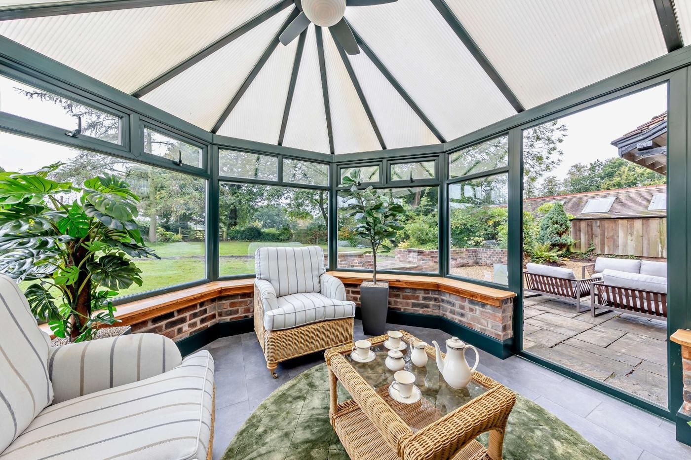 A conservatory with a glass ceiling, wicker furniture, and a view of the garden.