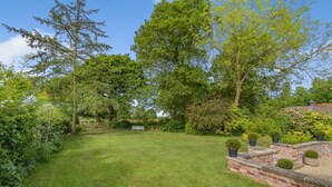 A well-maintained garden with a grassy lawn, a brick wall with planters, and a wooden bench. - 3 Bed in Thelwall (oc-c29954) (Warrington)