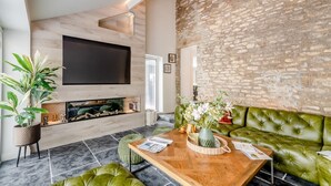A modern living room with a stone wall, a flat-screen TV, a fireplace, green leather sofa, and a wooden coffee table. - 4 Bed in Helmsley (oc-l29736) (Helmsley)