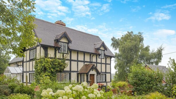 Ett hus i tudorstil med en symmetrisk fasad, flera skorstenar och en välskött trädgård med olika växter och blommor.