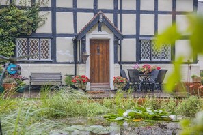 A traditional half-timbered house with a wooden door, a bench, and a table with chairs outside. - 2 Bed in Woofferton (oc-b29941) (Woofferton)