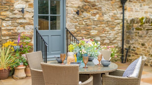 A stone building with a blue door, wicker furniture, and a table set with flowers and glassware.